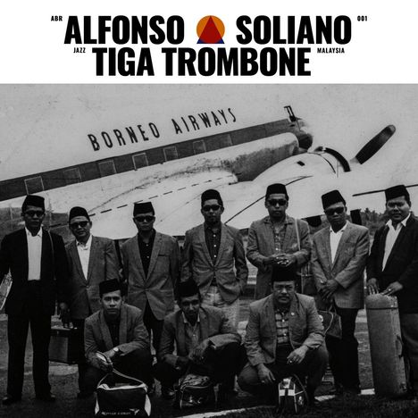 "ALFONSO SOLIANO TIGA TROMBONE", "BORNEO AIRWAYS". Gruppe Männer in Anzügen vor einem Flugzeug.
