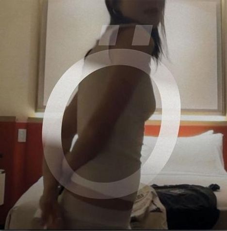 „Ö“ in großem, transparentem Stil. Eine Person steht in einem Zimmer mit Bett im Hintergrund.