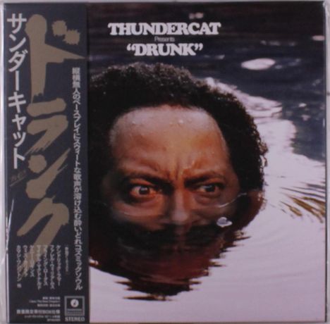 "THUNDERCAT presents 'DRUNK'. Japanische Schriftzeichen links. Ein Gesicht schaut knapp über die Wasseroberfläche."