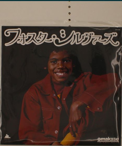 Ein fröhlicher Junge in roter Jacke, lächelt. Japanischer Text oben. "omakase" unten rechts.