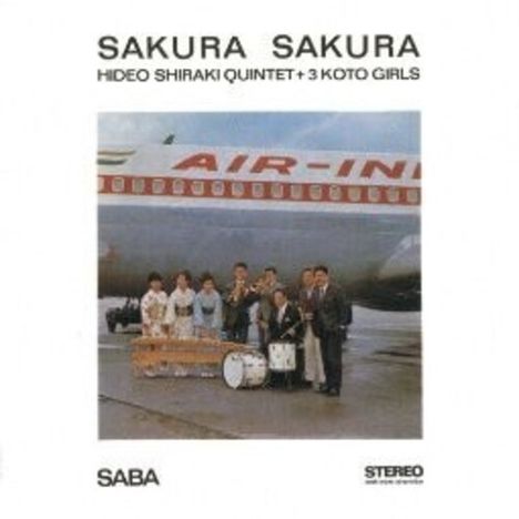 "Sakura Sakura" steht oben. "Hideo Shiraki Quintet + 3 Koto Girls" darunter. Menschen mit Musikinstrumenten vor einem Flugzeug.