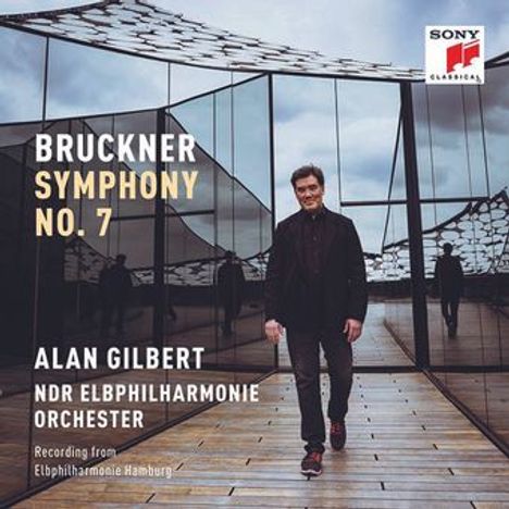 "Bruckner Symphony No. 7, Alan Gilbert, NDR Elbphilharmonie Orchester." Mann läuft vor moderner Glasarchitektur.