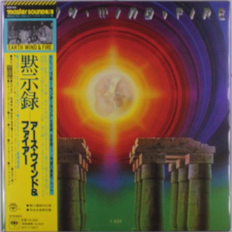 "Earth Wind & Fire" und "I AM". Illustration: Sonne im Zentrum, umgeben von bunten Ringen; Steinstrukturen im Vordergrund.