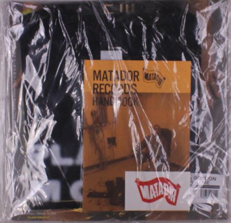 "MATADOR RECORDS HANDBOOK" steht auf einem gelben Hintergrund mit einem Matador-Logo. Verpackung ist faltig durch Plastikfolie.