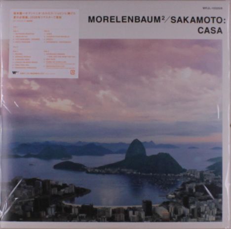Text: "MORELENBAUM² / SAKAMOTO: CASA". 

Sicht auf eine Küstenstadt bei Sonnenuntergang mit bergiger Umgebung.