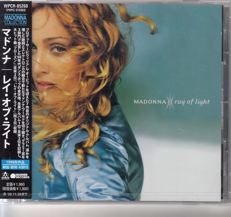 Text: "MADONNA ray of light". Links vertikaler japanischer Text. Frauenporträt, blondes Haar, blaue Kleidung.