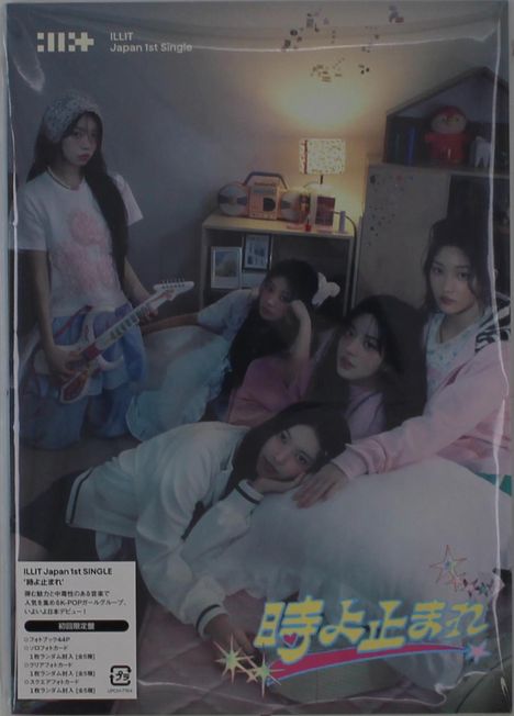 Oben steht "ILLIT Japan 1st Single". Fünf junge Frauen in einem gemütlichen Raum, umgeben von Kissen.