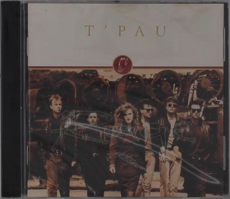 "T'PAU" steht oben. Darunter eine Gruppe von sechs Personen in dunkler Kleidung vor alten Eisenrädern.