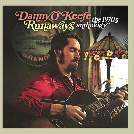 "Danny O'Keefe Runaways Anthology the 1970s." Ein Mann mit Gitarre sitzt neben einer bunten Lampe.