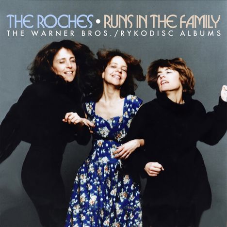 "The Roches • Runs in the Family. Drei Frauen lächelnd, eine in einem blauen Blumenmusterkleid, die anderen in Schwarz."