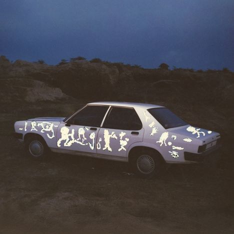 Das Bild zeigt ein weißes Auto in einer dunklen Umgebung mit leuchtenden Figuren auf der Karosserie.