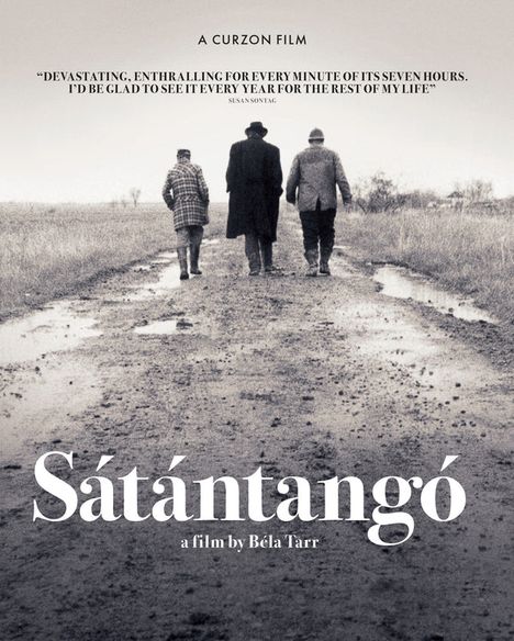 „Sátántangó“, ein Film von Béla Tarr. Drei Personen in Mänteln gehen eine schlammige, ländliche Straße entlang.