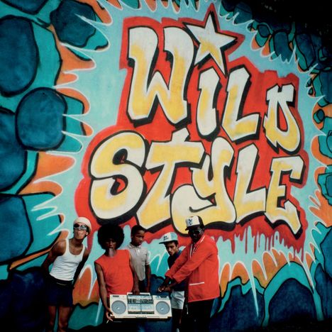 „Wild Style“ in gelber Graffiti-Schrift auf bunter Wand; fünf Personen mit Boombox stehen davor.
