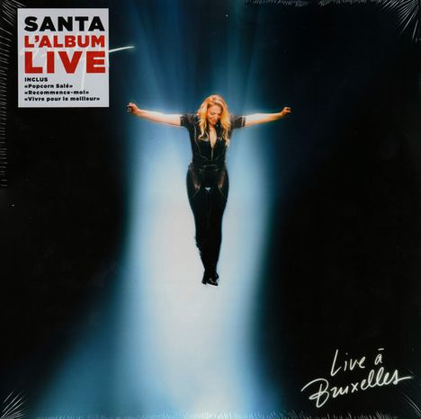 Text: "Santa L'album Live", "Live à Bruxelles". Person in schwarzem Outfit schwebt mit ausgebreiteten Armen im Lichtstrahl.