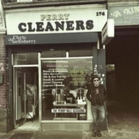 „Perry Cleaners“ steht als großes Schild über einem kleinen Laden. Ein Mann lehnt entspannt an der Fassade.