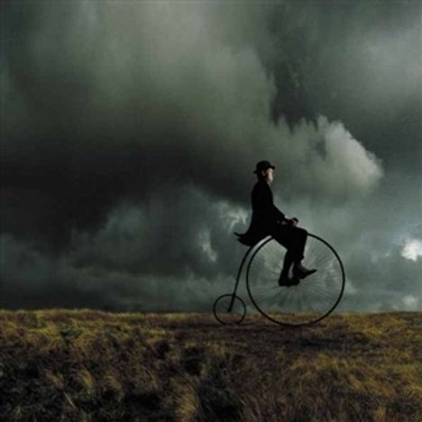 Ein Mann auf einem Hochrad fährt durch eine stürmische Landschaft unter dramatischen Wolken.