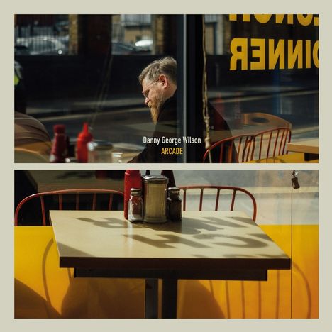 "Danny George Wilson" und "ARCADE" sind zentral sichtbar. Szene in einem Café, Mann neben einem Tisch mit Gewürzen, gelbes Interieur.