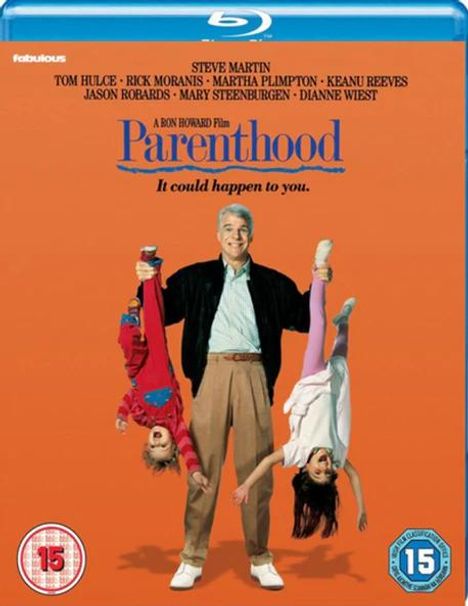 Text: "Parenthood. It could happen to you." Steve Martin hält humorvoll zwei Kinder kopfüber auf einem orangen Hintergrund.