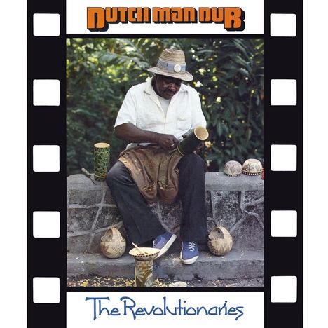 "Dutch Man Dub" und "The Revolutionaries". Ein Mann in weißem Hemd bearbeitet ein Holzobjekt, umgeben von Körben.