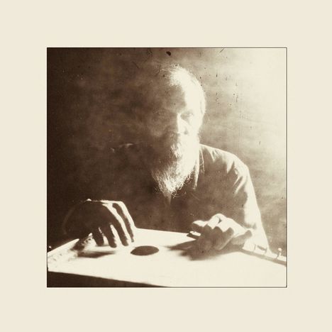 Keine erkennbaren Texte. Ein Mann mit Bart spielt ein Musikinstrument in einem schattigen Raum.