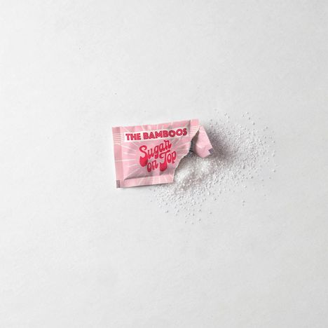 Der Text „THE BAMBOOS Sugar on Top“ steht auf einem rosa Zuckertütchen, aus dem Zucker rieselt.