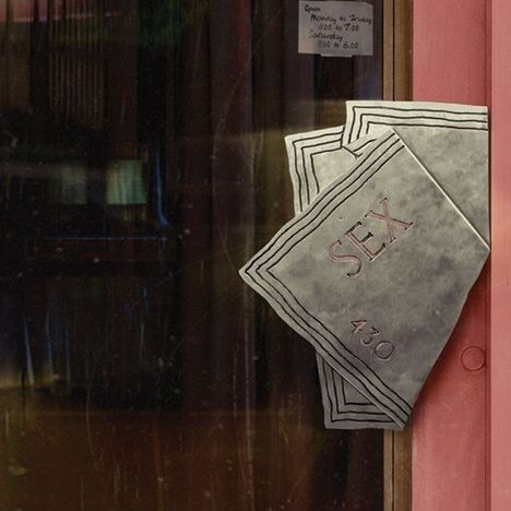 Ein Schild zeigt die Öffnungszeiten: Montag bis Freitag 11-19 Uhr, Samstag 11-18 Uhr. Eine Metallplatte mit "SEX".
