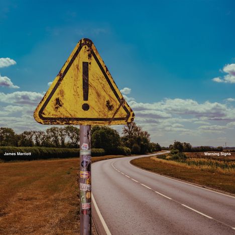 "James Marriott", "Warning Signs". Ein altes, dreckiges gelbes Warnschild vor einer Landstraße und blauem Himmel.