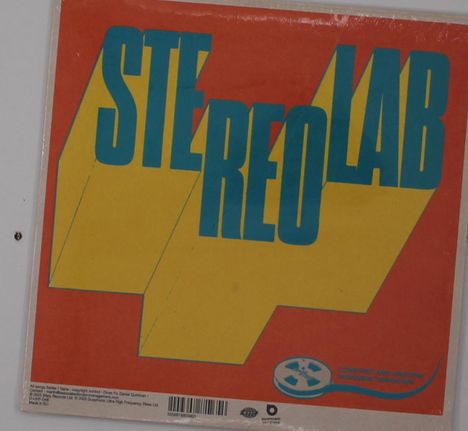 Der Text "STEREOLAB" ist in großen, blauen Buchstaben diagonal auf einem gelben Hintergrund platziert.