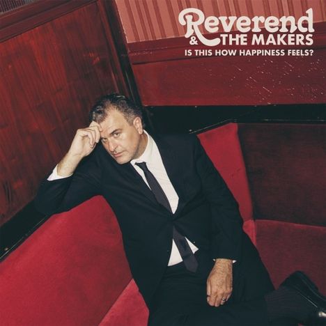 "Reverend & The Makers. Is This How Happiness Feels?" Ein Mann in Anzug sitzt nachdenklich auf einem roten Sofa.