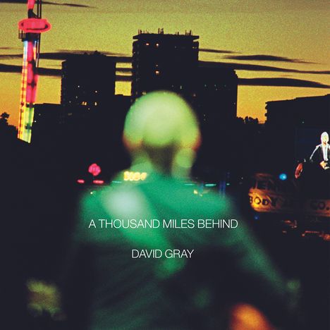 "A THOUSAND MILES BEHIND, DAVID GRAY" vor unscharfem grünlichem Rücken, Abendhimmel mit Silhouetten von Gebäuden.