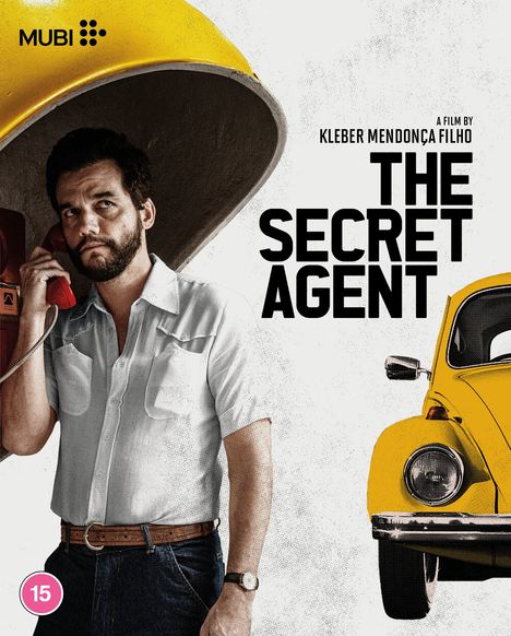 „THE SECRET AGENT“, Film von Kleber Mendonça Filho. Ein Mann telefoniert in einer gelben Telefonzelle, gelbes Auto rechts.