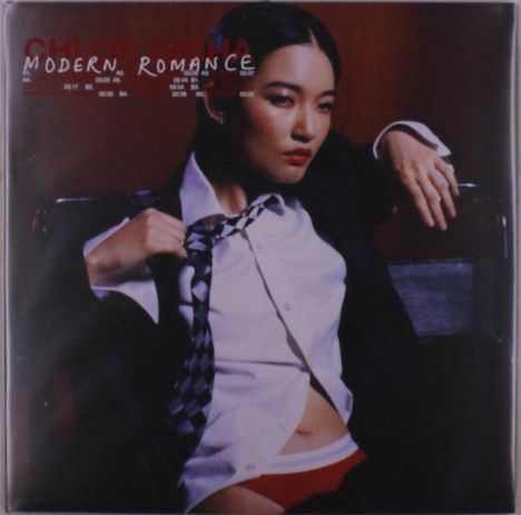 "Modern Romance" steht in weißer Schrift. Eine Frau in leicht geöffnetem Hemd und Krawatte sitzt lässig auf einem Stuhl.