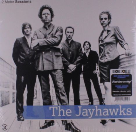 "2 Meter Sessions. The Jayhawks." Fünf Personen in formeller Kleidung stehen auf einem Holzboden.