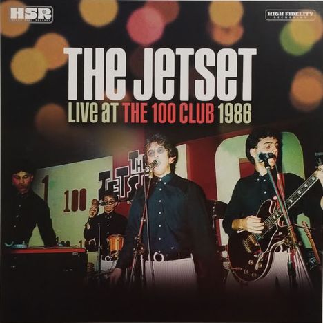 "The Jetset Live at The 100 Club 1986" in großen Buchstaben. Bandmitglieder auf einer Bühne mit Instrumenten.