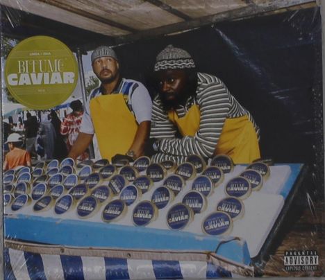 "Bitume Caviar" steht auf einer gelben Tafel. Zwei Männer in gestreifter Kleidung und gelben Schürzen stehen am Marktstand mit Konserven.