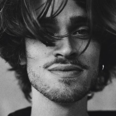 Ein Schwarz-Weiß-Porträt eines lächelnden Mannes mit Bart und verwuschelten Haaren.