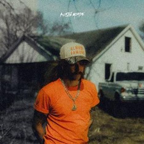 "AUSTIN MEADE" oben, Person in orange T-Shirt und Kappe vor einem alten weißen Haus im Hintergrund.