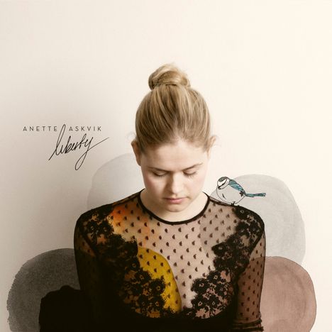 Text: "Anette Askvik Liberty" in stilvoller Schrift. Frau mit geschlossenem Blick in schwarzem Spitzenkleid, Vogel auf Schulter.