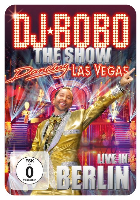 DJ BOBO, The Show, Dancing Las Vegas, LIVE IN BERLIN. Ein lächelnder Mann im goldenen Anzug zeigt auf etwas.