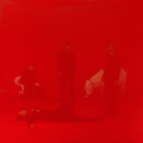 Rotes, verschwommenes Bild; schemenhaft erkennbare Menschen und ein weißes Pferd. Surreal und mystisch.