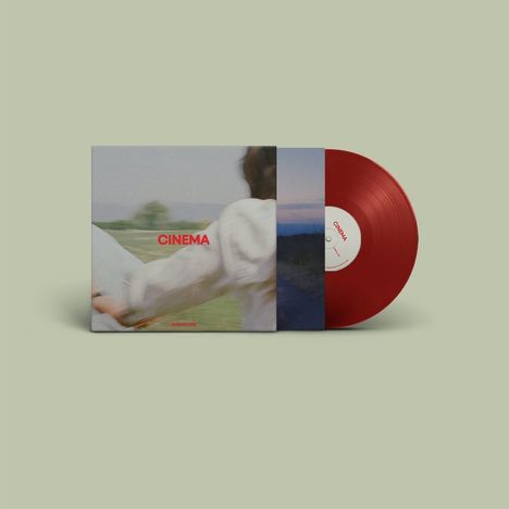 „CINEMA“ in roter Schrift auf einem Plattencover, daneben eine rote Vinyl-Schallplatte. Verschwommene Landschaft im Hintergrund.