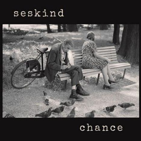 Text oben: "seskind". Text unten: "chance".  
Ein älteres Paar sitzt auf einer Parkbank, umgeben von Tauben.