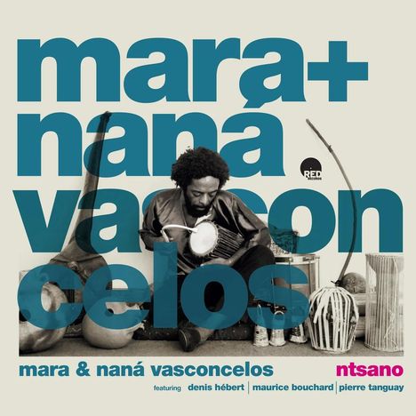 Aufschrift: "mara+ nana vasconcelos". Ein Mann spielt ein Perkussionsinstrument, umgeben von Musikinstrumenten.
