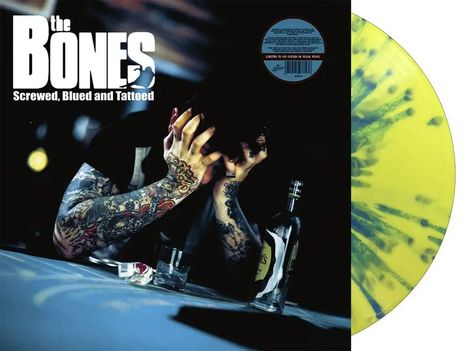 „The Bones, Screwed, Blued and Tattooed“. Tätowierte Person verdeckt Gesicht mit Händen, bläuliche Beleuchtung.