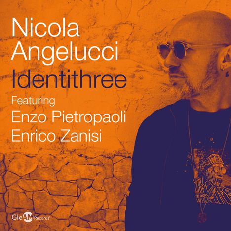 Texte: "Nicola Angelucci Identithree, Featuring Enzo Pietropaoli Enrico Zanisi." Eine Person mit Sonnenbrille vor einer Wand.