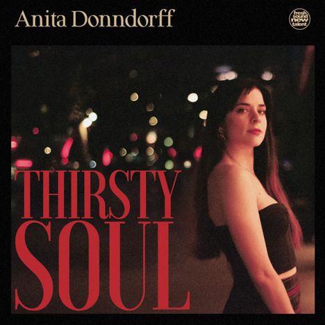 Anita Donndorff, Thirsty Soul. Eine Frau in Abendkleidung blickt in die Kamera, verschwommene Lichter im Hintergrund.