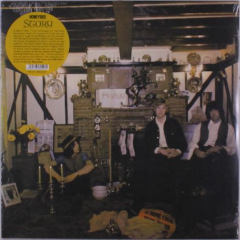 Text: "HONEYBUS STORY". Drei Männer sitzen in einem nostalgisch eingerichteten Raum mit Kamin, Blumen und antiken Gegenständen.