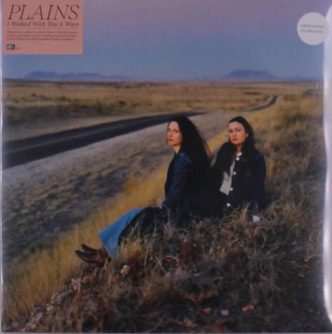 Text: "PLAINS, I Walked With You A Ways". Zwei Frauen sitzen in Gras neben einer Straße, Berge im Hintergrund.