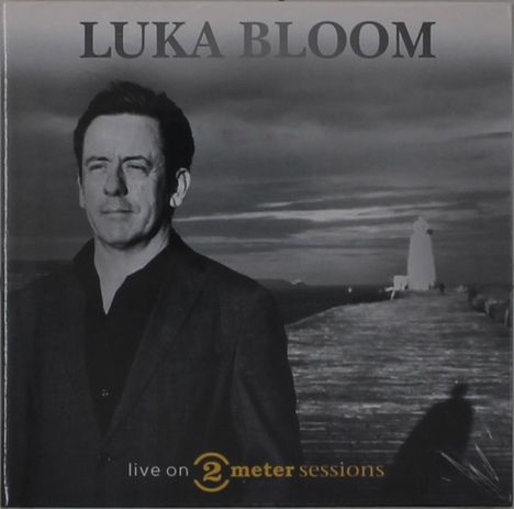 "LUKA BLOOM" oben, "live on 2 meter sessions" unten. Mann im Anzug auf einem Steg mit Leuchtturm im Hintergrund.