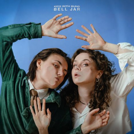 "KIDS WITH BUNS BELL JAR" steht oben, zwei Personen posieren spielerisch mit erhobenen Händen vor blauem Hintergrund.